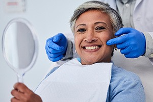 Woman smiling while holding small mirror with dentist